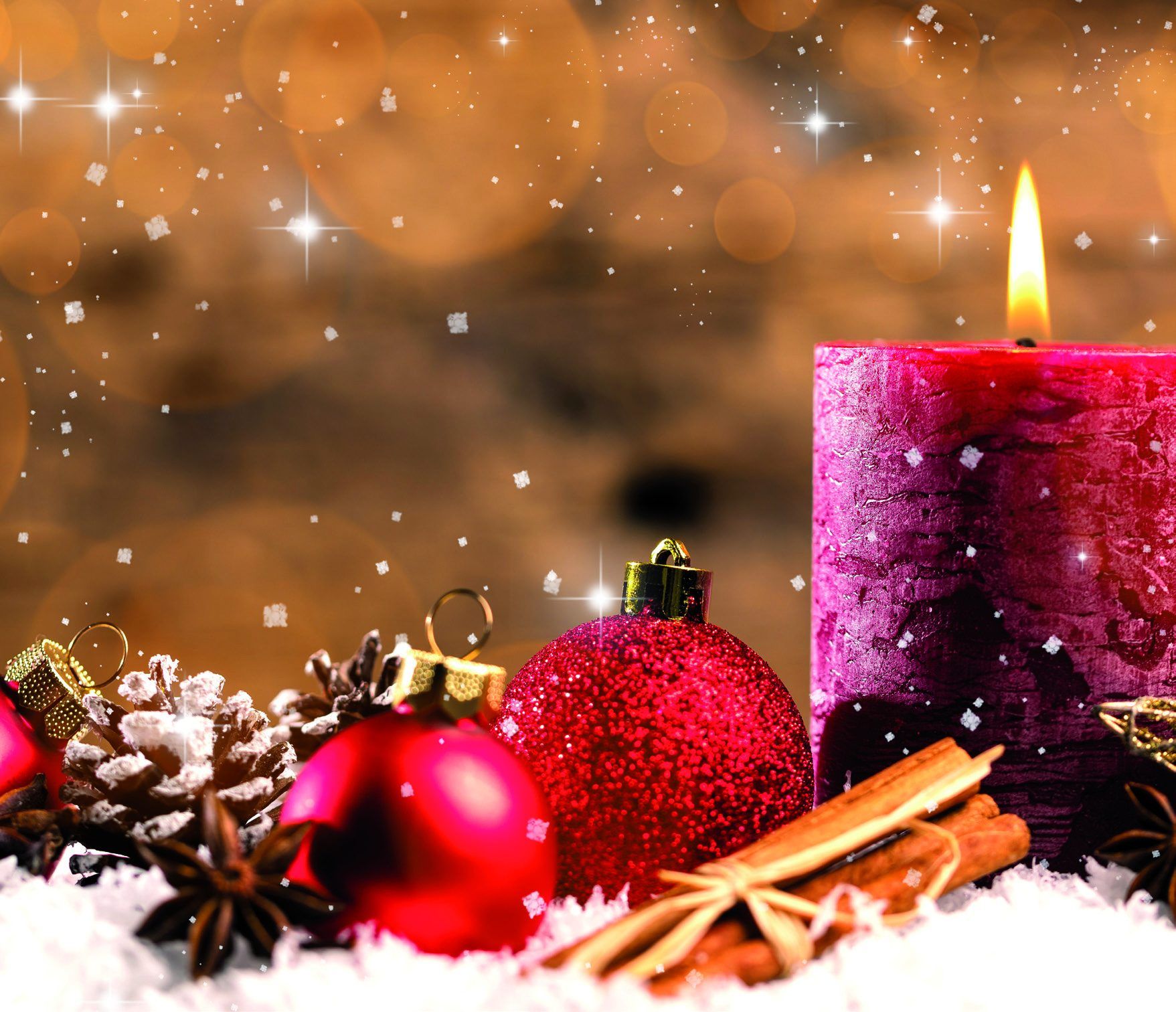 Brennende pinkfarbene Kerze mit roten Christbaumkugeln, Zimtstangen, Sternanis und Zapfen im Schnee