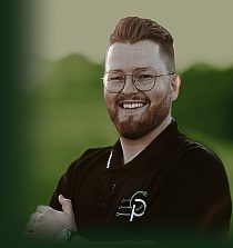 Lächelnder Mann mit Brille und Bart im schwarzen Firmenpolo vor grünem Hintergrund