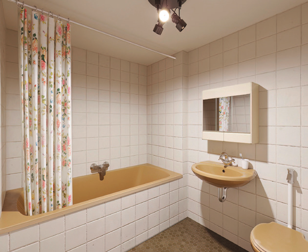 Altes Badezimmer mit beiger Badewanne, Blumenduschvorhang, Waschbecken und weißen Fliesen