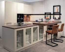 Küche mit Kochinsel, Holz-Oberschränken, Backofen und Glasvitrine unter der Arbeitsplatte.