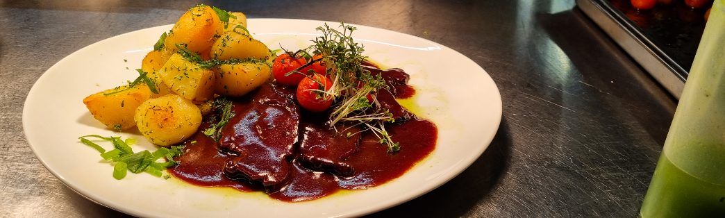 Teller mit Fleisch in dunkler Sauce, Bratkartoffeln, Kirschtomaten und Kresse