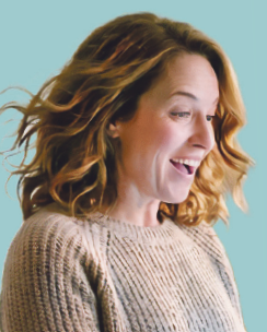 Lachende Frau mit lockigem Haar in beigem Strickpullover