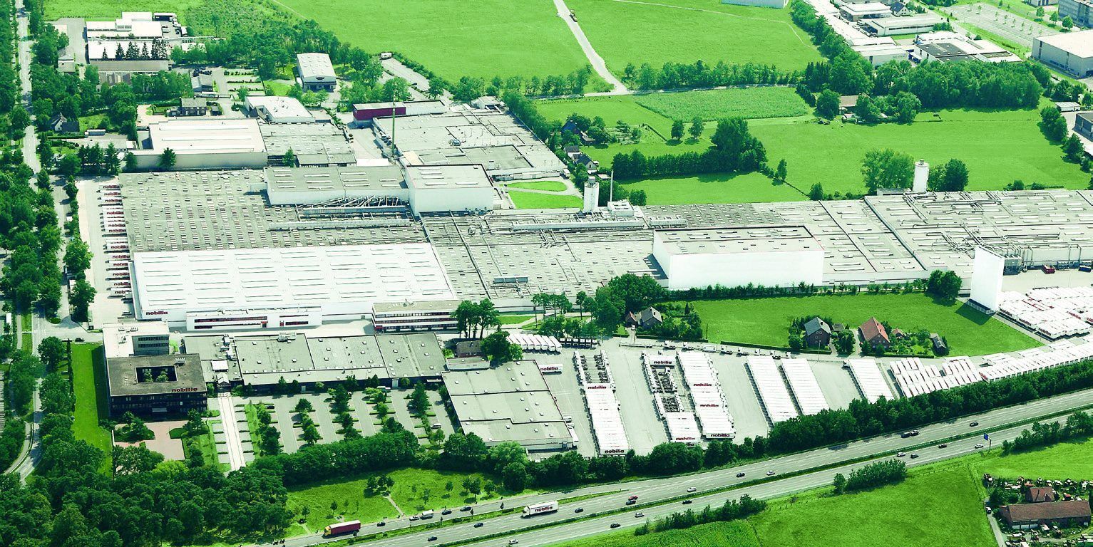 Luftbild eines Produktionsstandorts mit Hallen, Autobahn und Grünflächen
