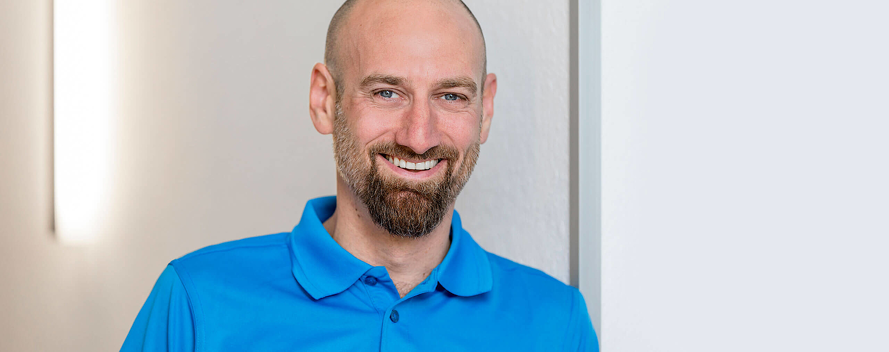 Portraitfoto von Malte Mittermeier, lächelnd im blauen Poloshirt vor heller Wand