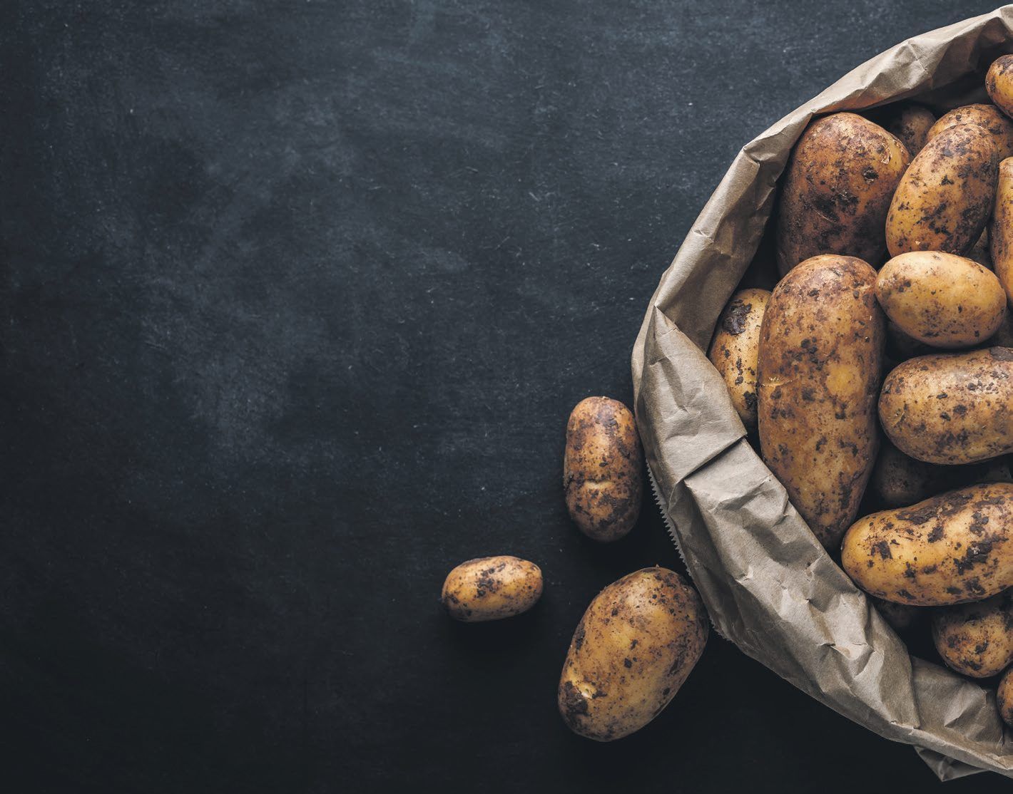 Kartoffeln in einer braunen Papiert&uuml;te auf dunklem Schiefer
