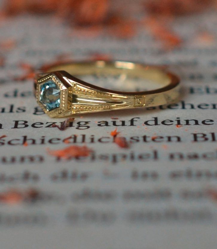 Goldring mit hellblauem Edelstein liegt auf einer aufgeschlagenen Buchseite
