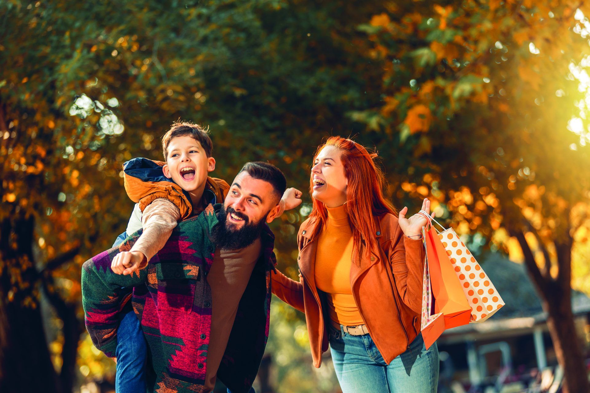 Lachende Familie mit Kind auf den Schultern und Einkaufstüte im herbstlichen Park